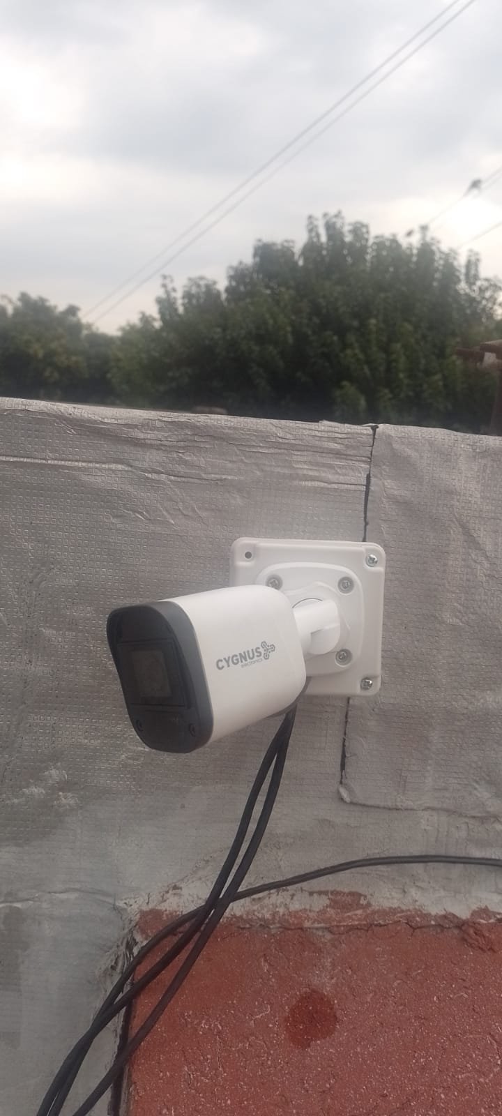Cámara bullet Cygnus blanca instalada en lo alto de una pared de concreto texturizado sobre su respectiva caja de conexiones estanca